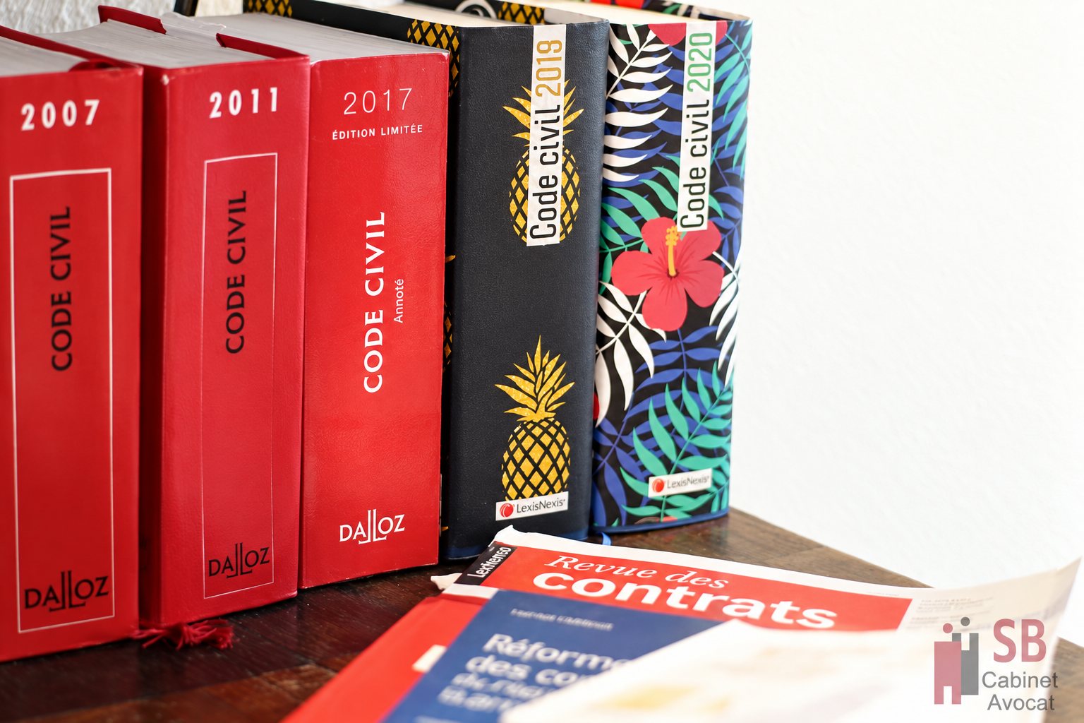Codes civils à la couverture rouge alignés sur une table en bois, avec une Revue des contrats ouverte au premier plan.